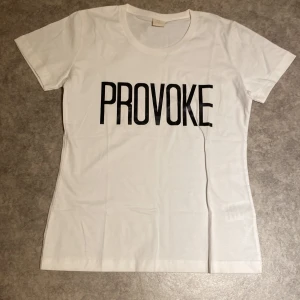 Vit t-shirt med svart tryck från Jotex - Vit t-shirt från Jotex med stort svart texttryck 'PROVOKE' på bröstet. Klassisk rund halsringning och korta ärmar. Tillverkad i mjuk bomull för en skön känsla och enkel stil.