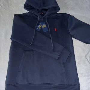 Marinblå hoodie från Polo Ralph Lauren - Säljer en marinblå hoodie från Polo Ralph Lauren med klassisk röd broderad logga på bröstet för 1500 men priset kan diskuteras. Tröjan har huva med snörning, känguruficka och är tillverkad i 100% bomull för en skön känsla. Perfekt för dig som gillar stilrena och tidlösa plagg.St M men passar mer S