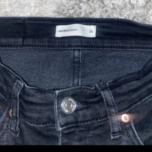 Svarta bootcut jeans från Perfect Jeans - Svarta jeans från Perfect Jeans i storlek 34. Modellen har klassisk femficksdesign, knapp och dragkedja framtill samt bootcut-ben som ger en snygg siluett. Jeansen är tillverkade i ett stretchigt denimtyg för skön passform.