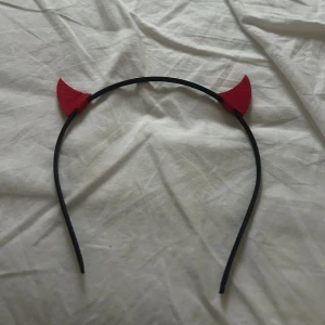 Diadem med röda djävulshorn - Säljer ett svart diadem med röda djävulshorn i filtmaterial. Perfekt accessoar för temafest eller halloween. Diademet är smalt och flexibelt, och hornen är spetsiga och sitter stadigt på båda sidor.
