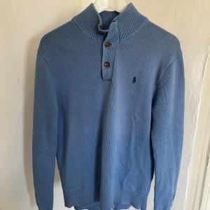 Blå stickad tröja Polo Ralph Lauren - Säljer en blå stickad tröja från Polo Ralph Lauren med hög krage och tre knappar framtill. Tröjan har lång ärm, ribbade muddar och den klassiska broderade loggan på bröstet. Perfekt för lager-på-lager under kyliga dagar. Hör av dig on du har frågor!🙌