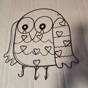 Svart uggleformad väggkrok i metall - Säljer en svart väggkrok i form av en uggla, tillverkad i metall. Ugglan har hjärtformade detaljer och tre krokar längst ner, perfekt för att hänga upp nycklar eller accessoarer. Söt och dekorativ detalj till rummet.