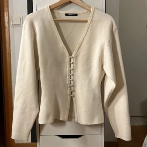 Vit kofta med knappar från Gina Tricot - Superfin vit kofta från Gina Tricot i mjukt material. Koftan har v-ringning, långa ärmar och snygga klädda knappar framtill. Perfekt att slänga över en topp för en chill look. Inga defekter!