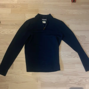Mörkblå stickad half zip-tröja Pier One - Mörkblå stickad tröja från Pier One med half zip-dragkedja och hög krage. Tröjan har lång ärm och ribbade muddar vid hals, ärmslut och nederkant. Perfekt för lager-på-lager och chill stil.