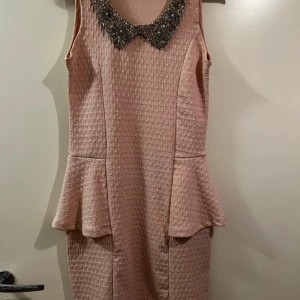 Rosa klänning från Robin - Säljer en superfin rosa klänning i storlek S. Den har en snygg textur och en peplumdetalj i midjan som ger en elegant touch. Klänningen är ärmlös och perfekt för festliga tillfällen. Den har en dekorativ krage med pärlor som ger extra glamour. Passar perfekt till vår och sommar! Är endast använd vid ett par tillfällen. Högst 4 tillfällen. Så den är ren och i gott skick 
