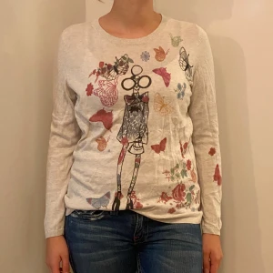 Beige tröja med tryck från Oui - Säljer en superfin beige tröja från Oui i storlek 40. Den är gjord av 100% bomull och har ett coolt tryck med blommor och fjärilar. Perfekt för både vår och höst! Tröjan har långa ärmar och en normal passform. Skön och stilren för vardagsbruk.