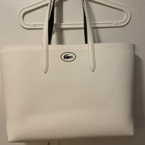 Väska LACROSTE  - Köptes för 1600kr, endast ett litet märke på undersidan av väskan som förmodligen går bort med städmedel! Vit på utsidan och mörkgrönaktig på insidan. Köptes på ”väskan”