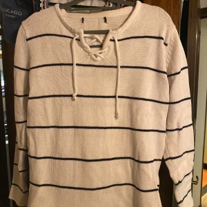 Randig stickad tröja med knyt - Säljer en superfin vit stickad tröja med mörkl blås ränder. Den har långa ärmar och en snygg knytning vid halsen som ger en extra detalj. Perfekt för både vår och höst när det är lite kyligare ute. Passar till både jeans och kjol!💕Det står ingen storlek men sitter bra på mig som brukar ha S