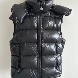 Moncler bormes down väst  - Snygg svart dunväst från Moncler med hög krage och dragkedja. Västen har en quiltad design och Moncler-logga på bröstet. Perfekt för kyligare dagar. Pm för fler frågor storlek skulle jag säga är M/L NFC och QR kod fungerar, Priset är diskuterbart