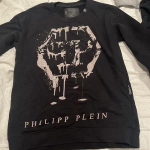 Svart tröja från Philipp Plein - Snygg svart tröja från Philipp Plein med ett unikt tryck på framsidan. Tröjan har långa ärmar och en klassisk passform. Perfekt för en stilren look.