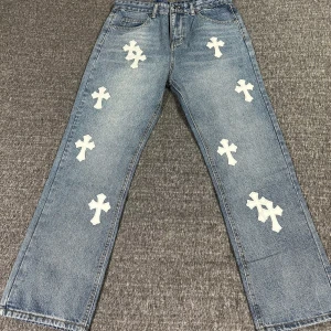 Chrome hearts jeans - Snygga blå jeans med unika vita korsdetaljer. Byxorna har en loose passform och är perfekta för en avslappnad stil. De har en klassisk femficksdesign och är tillverkade i jeansmaterial.