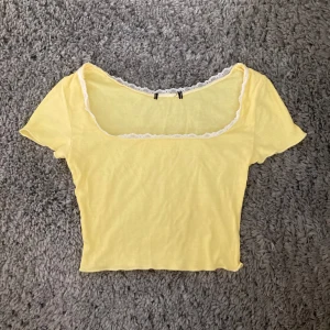 Gul topp med spetsdetaljer - Kortärmad croppad gul topp med spetskant. Toppen är sällan använd och är därför i gott skick. Uppskattas till strl S. Klicka gärna på köp nu och meddela för eventuella frågor. :)