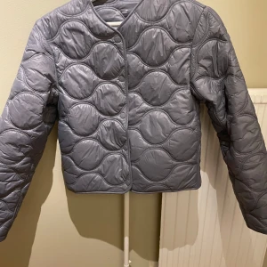 Grå quiltad jacka - Snygg grå quiltad jacka med rund hals och tryckknappar. Perfekt för kyliga dagar med sin stilrena design och bekväma passform.