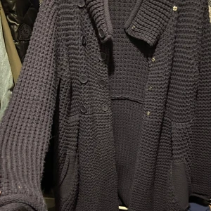 Mörkblå stickad kappa från French Connection - Säljer en snygg mörkblå stickad kappa från French Connection. Den har en dubbelknäppt design med stora knappar och praktiska fickor framtill. Perfekt för kyliga dagar med sin långa ärm och mysiga material.