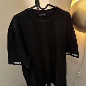 Svart t-shirt från Axel Arigato - Snygg svart t-shirt från Axel Arigato med textdetaljer på ärmarna. Tillverkad i 100% bomull för en bekväm passform. Perfekt för en stilren look.