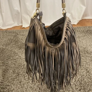 Mörkgrön axelväska med fransar från H&M - Snygg mörkgrön axelväska från H&M med långa fransar och dragkedja. Rymmer ganska mycket samt har flera fack