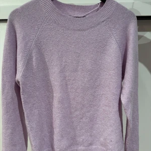 Ljuslila stickad tröja - Mysig ljuslila stickad tröja med rund hals och långa ärmar. Perfekt för kyliga dagar och ger en stilren look. Passar bra till både jeans och kjol.