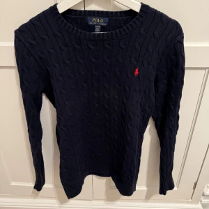 Mörkblå stickad tröja från Ralph Lauren - Säljer en snygg mörkblå stickad tröja från Ralph Lauren med det klassiska röda logotypbroderiet på bröstet. Tröjan har en rund halsringning och långa ärmar, perfekt till exempelvis ett par jeans i vardagen! Pris kan diskuteras, bara att höra av dig vid funderingar!🤩🤩