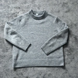 Grå stickad tröja Arket - Säljer en stilren grå stickad tröja från arket med rund hals och ribbade muddar. Perfekt för kyliga dagar och enkel att matcha med olika outfits. Den är Xs men passar som S-M
