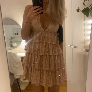 Glittrig guld klänning - Snygg glittrig guld klänning med volanger och djup v-ringning. 