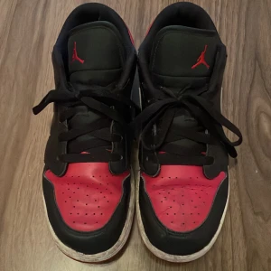 Nike Air Jordans i svart och röd - Säljer ett par klassiska Nike Air Jordans i svart och röd med vit sula. Skorna har snörning och den ikoniska Jumpman-loggan på plösen. Perfekta för dig som älskar en sportig och stilren look.