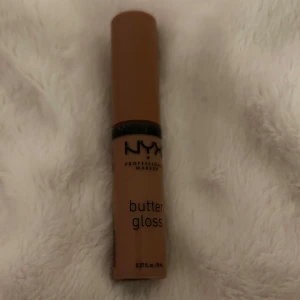 NYX Butter Gloss - Säljer ett NYX Butter Gloss i en varm brun nyans. Perfekt för att ge läpparna en mjuk och glansig finish. Enkel att applicera och ger en långvarig effekt.