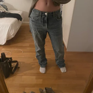 Blå jeans med baggy passform - Säljer ett par klassiska blå jeans med lite baggy passform. De har en rak stil och är perfekta för en avslappnad look. Jeansen har en knapp och dragkedja framtill.