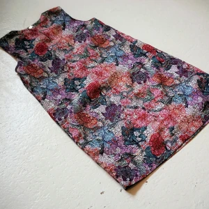 Färgglad ärmlös klänning från H&M - Säljer en färgglad ärmlös klänning från H&M med ett unikt blommigt mönster i lila, rött och blått. Klänningen har en dragkedja bak och en rund halsringning. Perfekt för en somrig look!