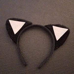 Svart diadem med kattöron - Snyggt svart diadem med kattöron, perfekt för en rolig och lekfull look. Öronen har vita triangulära detaljer som ger en extra touch. Passar bra för fester eller temadagar.