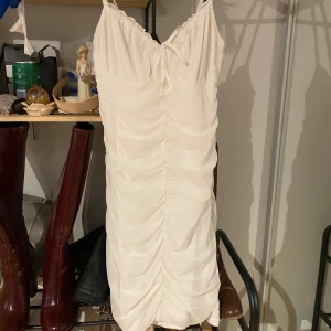 Vit klänning med rynkdetaljer - Elegant vit klänning med smala axelband och rynkdetaljer längs framsidan. Perfekt för en stilren look.