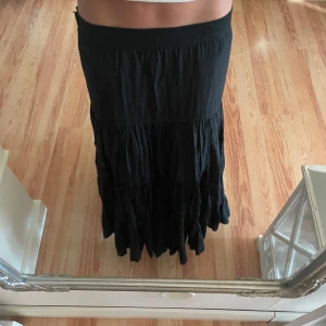 Svart långkjol från Zoul - Säljer en svart långkjol från Zoul som är knappt använd, egentligen som ny. Kjolen har en elastisk midja och ett flödande, volangliknande fall som ger en bohemisk känsla. Perfekt till sommaren!💕Storlek M men skulle säga att den är som S