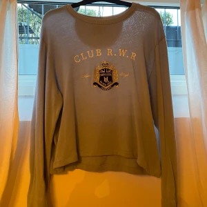 Ljusblå tröja från Henri Lloyd - Säljer en ljusblå tröja från Henri Lloyd med texten 'CLUB R.W.R' och ett stiligt emblem på framsidan. Tröjan har långa ärmar och en rund halsringning, uppsydd så den passar en L fast har långa ärmar. Perfekt för en avslappnad stil.