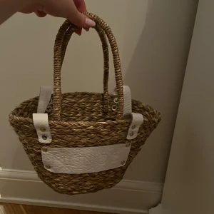 Núnoo beach-bag, mini  - SÅ fin stråväska/beach-bag från Núnoo med vita läderdetaljer och handtag. Väskan är i nyskick då den enbart är använd ett fåtal gånger! 