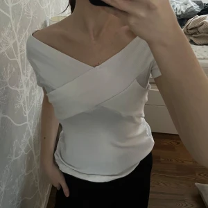 Vit topp - Snygg vit kortärmad topp med korsad design framtill. Går även att ha som offshoulder. Toppen har en ribbad struktur och en tight passform som framhäver figuren. Perfekt för en stilren look😍