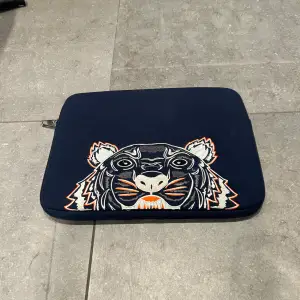 Snygg och stilren mörkblå datorväska från Kenzo med ett coolt tigerhuvud broderat på framsidan. Väskan har en dragkedja och är perfekt för att skydda din laptop. Den är gjord i ett slitstarkt material och har en broderad logga på baksidan. Perfekt för både skola och jobb!