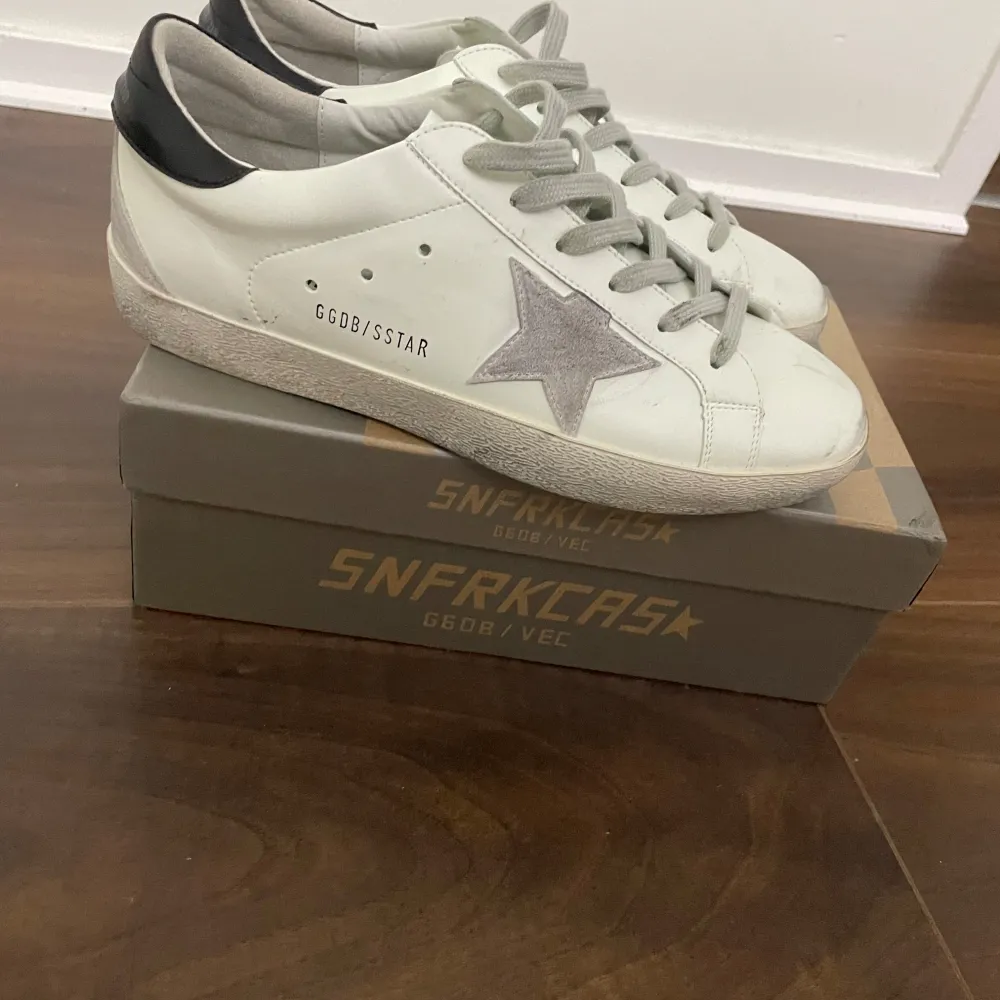 Säljer ett par vita Golden Goose sneakers i bra skick. De har en grå stjärna på sidan och svarta detaljer vid hälen. Skorna är använda 2-3 gånger och väldigt fräscha skorna är även 100%äkta och har ett digitalt kvittobevis så passa på för det är även väldigt lågt pris för att vara Golden goose. Med skorna tillkommer även en box och en påse så passa på!!. Skor.