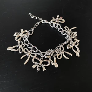 Handgjort Silverfärgat armband med rosetter - Säljer ett superfint silverfärgat armband med flera små rosetter som hänger längs kedjan. Perfekt för att ge en söt och lekfull touch till din outfit. Armbandet har en justerbar kedja så det passar de flesta handleder. Perfekt för både vardag och fest! ✨