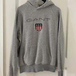 Grå hoodie från GANT - Säljer en grå hoodie från GANT i bra skick. Den är i storlek M och passar både kvinna och man. Tröjan fattas snören i luvan. Säljer hoodien då jag inte har användning av den längre. 