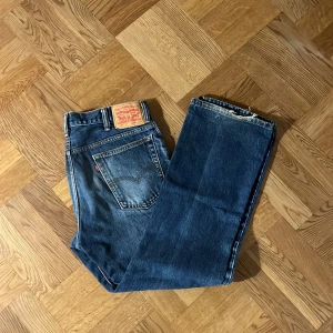 Blå jeans från Levi's - Säljer ett par klassiska blå Levi's jeans i bra skick. De har en bootcut/straight passform och är tillverkade i slitstarkt denim. Perfekta för vardagsbruk och kan enkelt matchas med olika outfits. Jeansens ikoniska lädermärke sitter på baksidan av midjan.