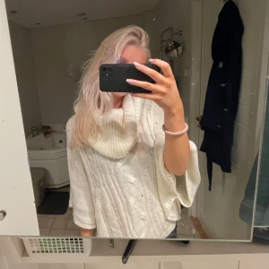 Vit stickad poncho - Säljer en supermysig vit stickad poncho med polokrage. Perfekt för kyliga höst- och vinterdagar. Den har en lös passform och är riktigt bekväm att ha på sig. Passar perfekt över en långärmad tröja eller blus. Perfekt för att hålla sig varm! 💫