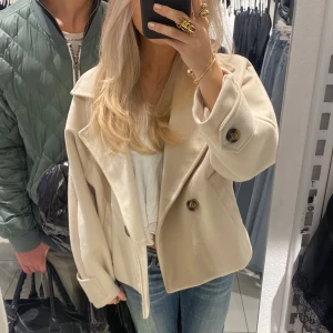 Beige kappa med stora knappar - Säljer en superfin beige kappa med stora knappar. Den är perfekt för höst och vår, med en stilren och klassisk look. Jackan har en lös passform och är långärmad, vilket gör den både bekväm och trendig. Perfekt för att hålla sig varm och snygg under kyligare dagar!
