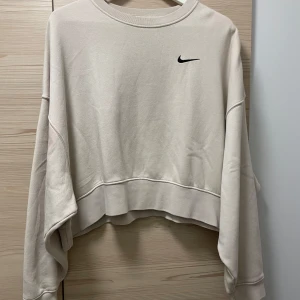 Beige sweatshirt från Nike - Säljer en superfin beige lite croppad sweatshirt från Nike. Den har en avslappnad passform med långa breda ärmar och en liten svart Nike-logga på bröstet. Använd ett fåtal gånger så i väldigt bra skick! Perfekt för en chill dag eller att matcha med dina favoritjeans. 🖤