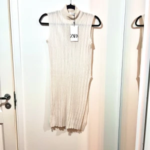 Beige ribbad topp från Zara - Säljer en stilren beige ribbad lång topp från Zara. Den är ärmlös och har en hög krage, slitz på vänster sida. perfekt för både vardag och fest. Plagget är oanvänt. 