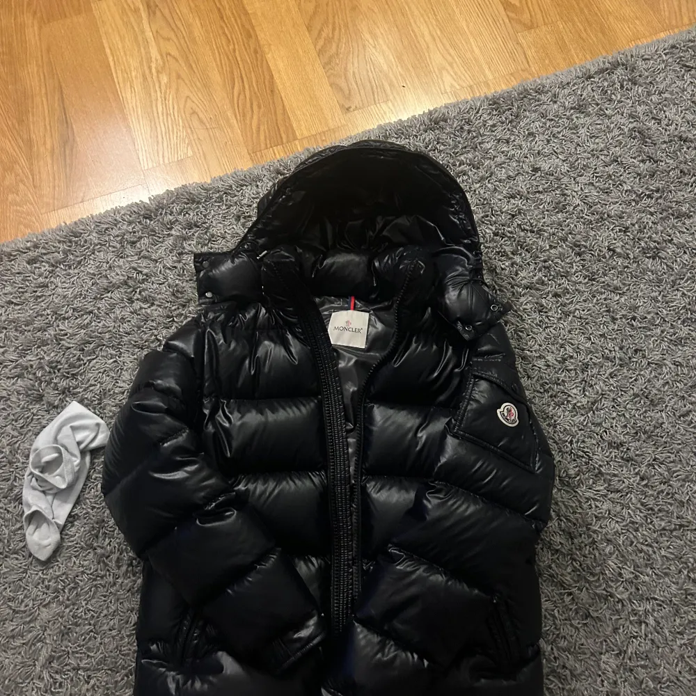 Säljer en snygg svart pufferjacka från Moncler i mycket bra skick. Jackan har en glansig finish och är perfekt för kalla dagar. Den har en dragkedja framtill och en huva för extra värme. Moncler-loggan sitter snyggt på ärmen. Perfekt för vintern! ❄️. Jackor.