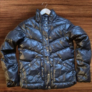 Svart pufferjacka från Hilfiger Denim - Säljer en snygg svart pufferjacka från Hilfiger Denim i bra skick. Jackan har en glansig yta med knappar och dragkedja framtill. Perfekt för kyliga dagar och ger en cool look. Passar både till vardags och lite finare tillfällen. 🖤