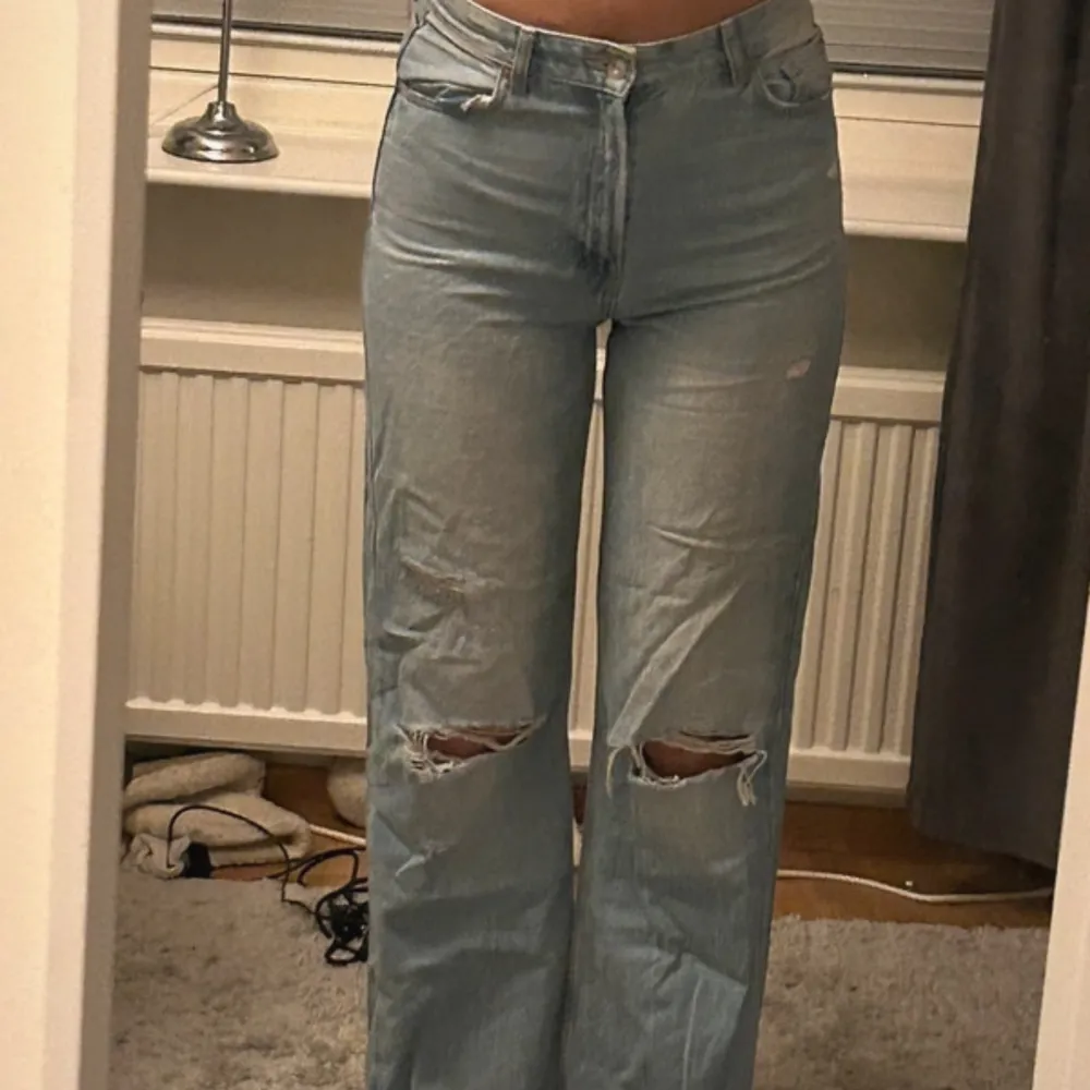 Säljer ett par ljusa jeans med coola slitningar på knäna. De har en hög midja och en straight passform som ger en avslappnad look. Perfekta för en casual outfit eller en dag på stan. Passar bra till sneakers eller boots!. Jeans & Byxor.