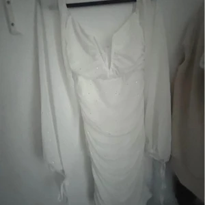 Vit glittrig klänning - Säljer en superfin vit klänning med glitterdetaljer. Den har en v-ringad design och långa ärmar som ger en elegant look. Perfekt för fest eller nyår! Klänningen är tight och framhäver figuren på ett snyggt sätt.