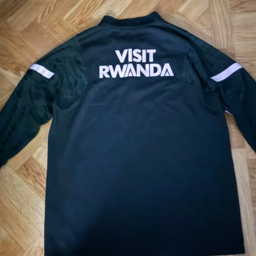 Säljer en svart långärmad PSG-tröja från Nike i mycket bra skick. Tröjan har vita detaljer och texten 'ACCOR LIVE LIMITLESS' på framsidan samt 'VISIT RWANDA' på baksidan. Perfekt för fotbollsfans som vill ha något stilrent och bekvämt. Passar både till träning och vardag.. T-shirts.