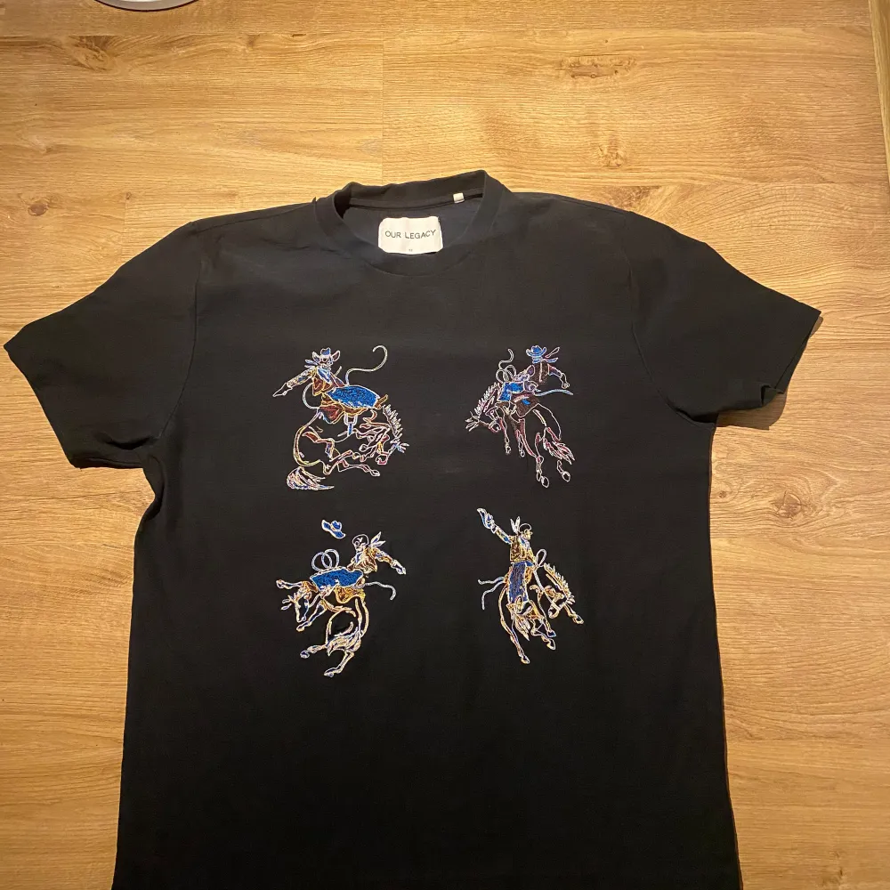 Säljer en svart t-shirt från Our Legacy i storlek 52. Den har ett coolt broderat mönster med cowboys i olika färger på framsidan. Perfekt för en avslappnad stil med en touch av western. T-shirten är kortärmad och gjord i ett mjukt material.. T-shirts.