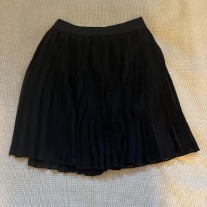 Svart plisserad kjol från NA-KD - Säljer en elegant svart plisserad kjol från NA-KD i storlek 32. Kjolen har en klassisk design med ett elastiskt midjeband för extra komfort. Perfekt för både vardag och festliga tillfällen. 🖤